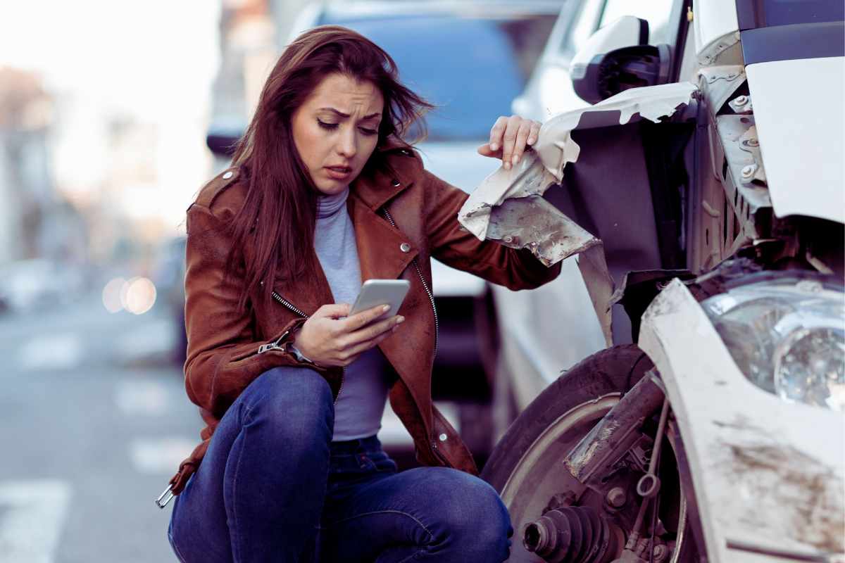 Woman inspecting damaged car and using phone after a crash in San Diego