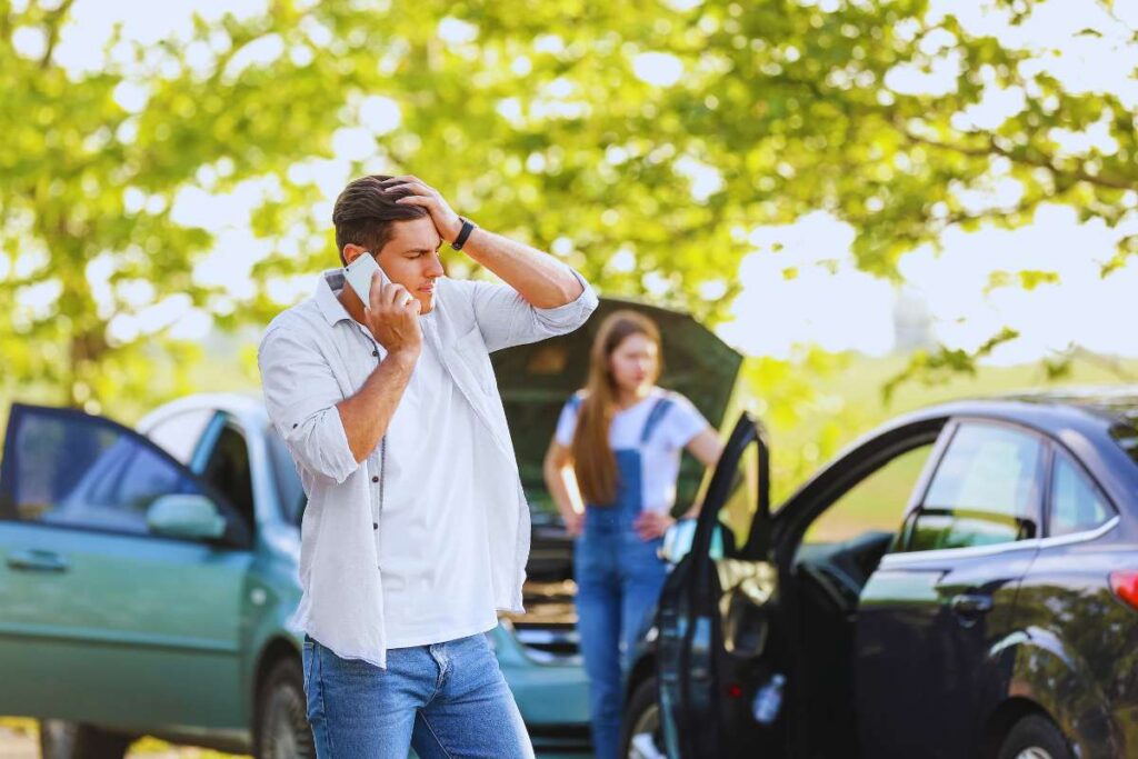 Man speaking on a phone while standing near damaged vehicles after a car accident, illustrating the uncertainty people face when dealing with insurance after a crash.