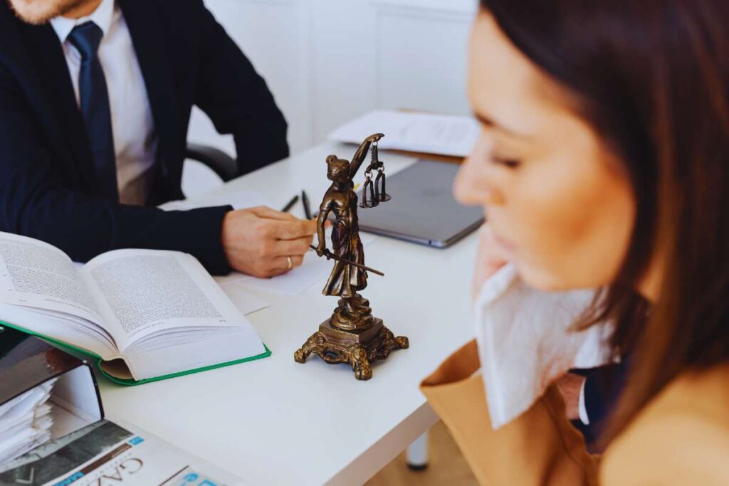 Injured woman meeting with a personal injury lawyer and reviewing legal documents after a San Diego rideshare accident, with the Lady Justice statue on the desk.