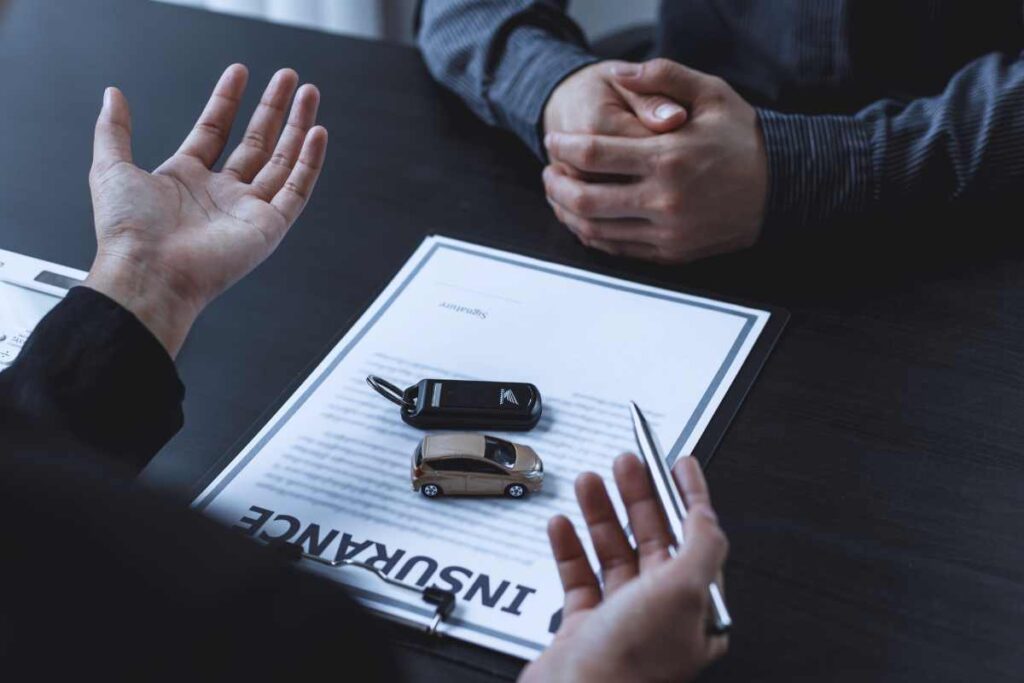 Two people meeting at a desk with car keys, model car, and insurance paperwork after an accident in San Diego