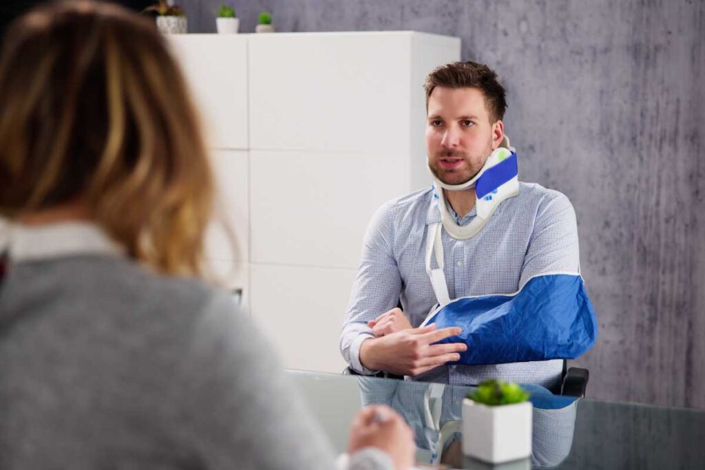 A man wearing a neck brace and arm cast speaks with a professional across a desk, illustrating how medical records and testimony support personal injury claims in San Diego.