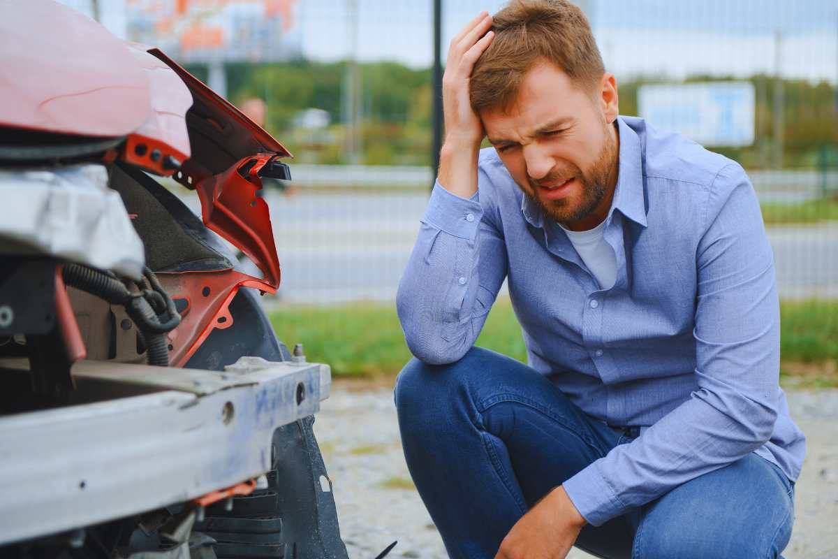 Man holding his head beside a damaged car after a rideshare accident, showing pain and confusion common in San Diego Uber and Lyft collisions.