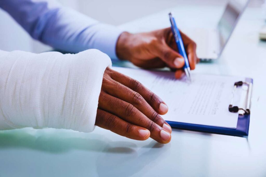 Person with an injured arm filling out paperwork for an Uber or Lyft insurance claim after a rideshare accident, documenting injuries and claim details