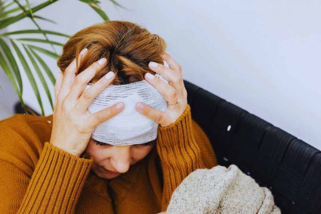 Person seated indoors holding their head with a bandage, illustrating post-accident discomfort and the importance of medical evaluation and documentation after a rideshare crash.