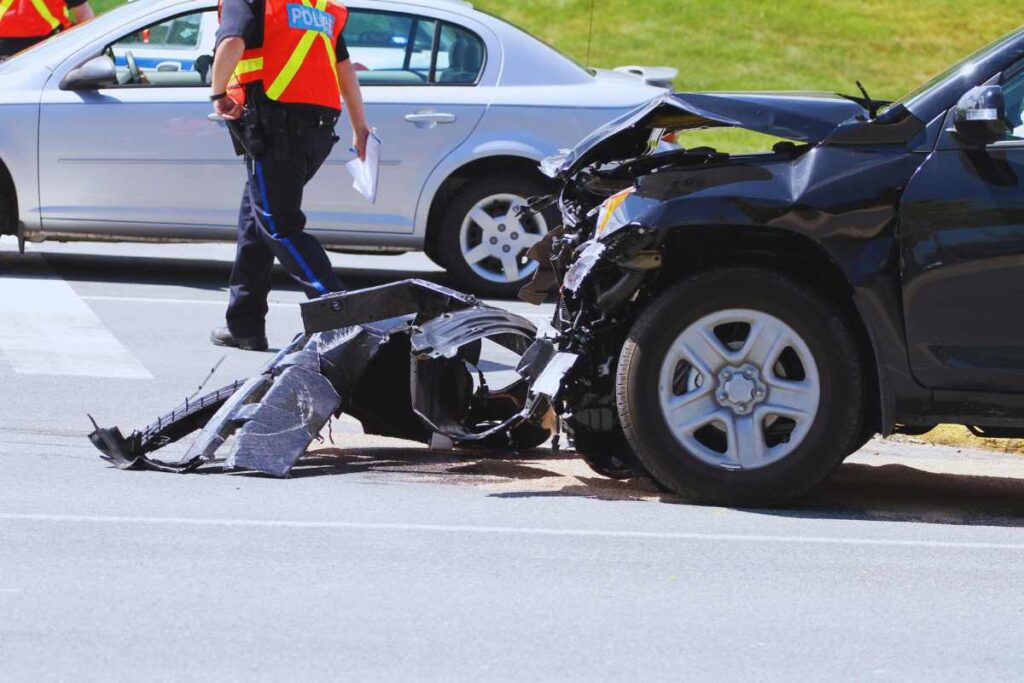 Black car with heavy front-end damage as police officer documents the accident scene in San Diego
