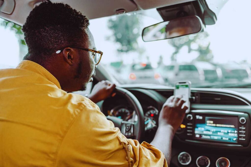 Rideshare driver looking at a navigation app while driving through traffic, showing how multitasking and app use can contribute to accident risk.