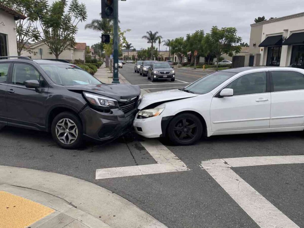 Two vehicles with front-end damage stopped at a Southern California suburban intersection with stucco buildings and crosswalk markings